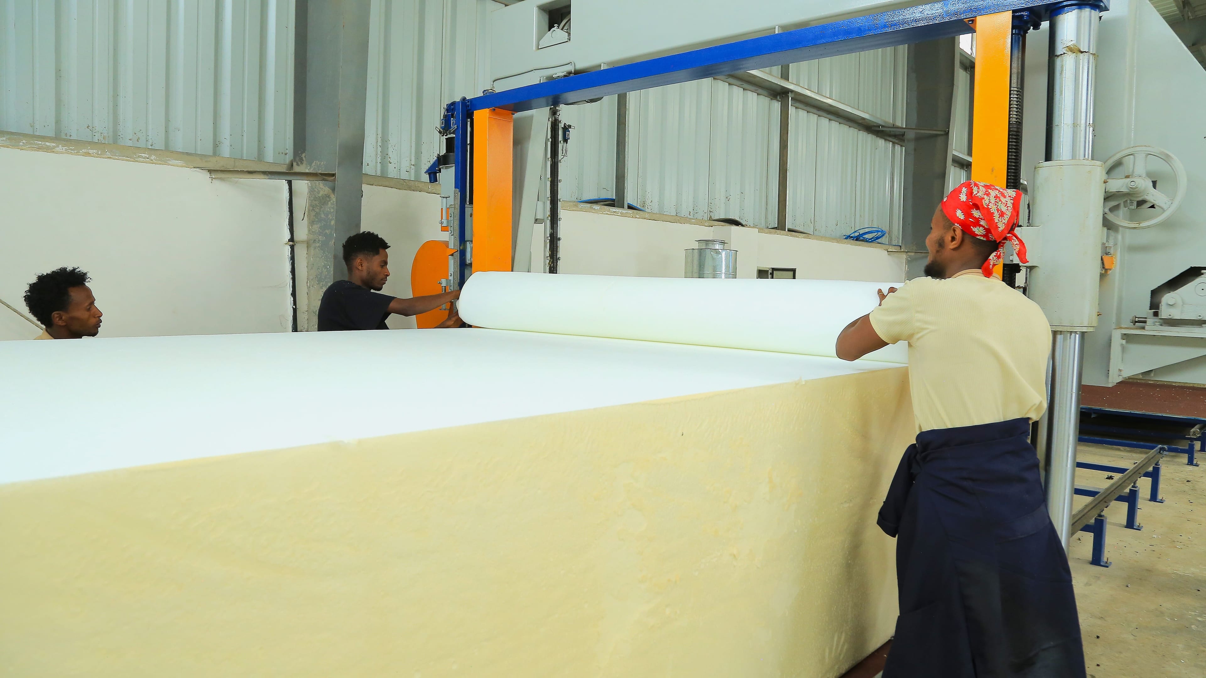 Foam sheet being sliced on a cutting machine, with workers rolling up the freshly cut sheet.